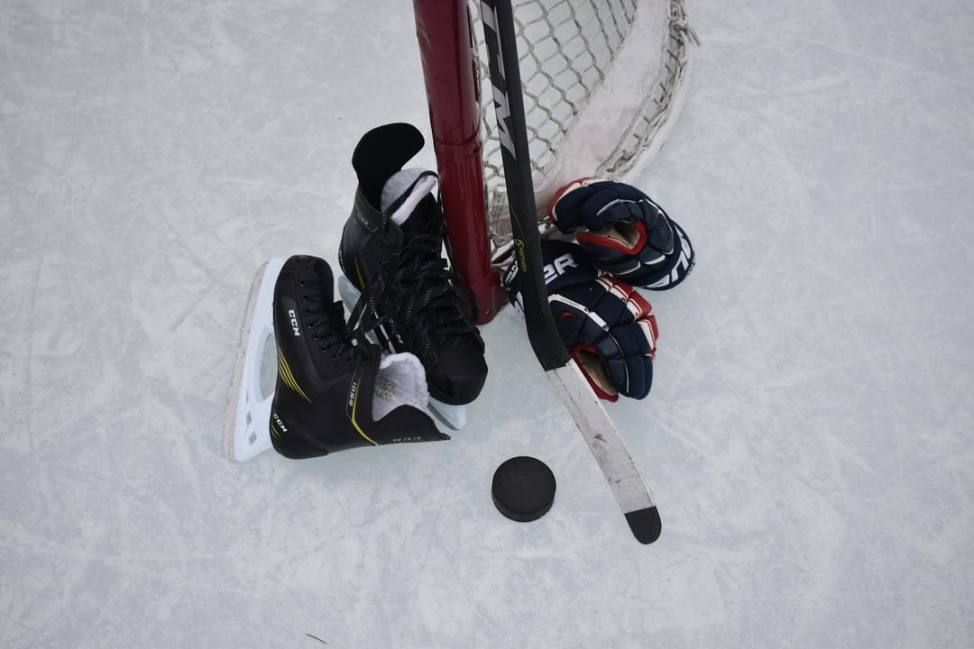 Skates, gloves and a stick resting against the net on outdoor ice