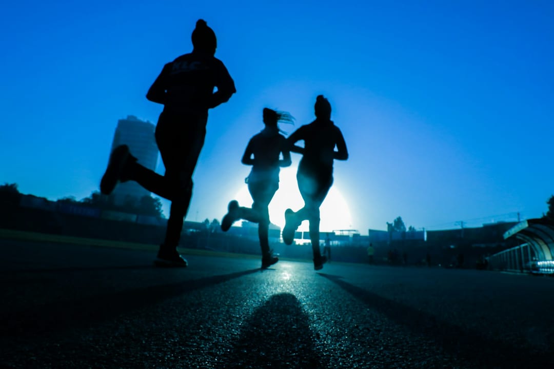 Three runners silhouetted against the sunrise on an open road