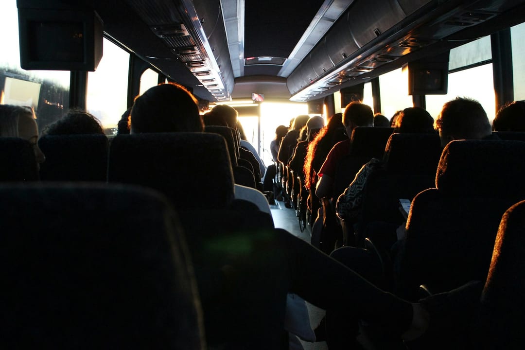 Rows of passengers on a bus riding into the evening sun